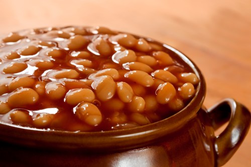 A close-up of a brown ceramic pot filled with baked beans in a rich sauce.