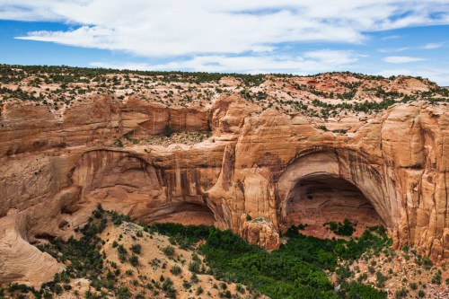 A stunning view of a large sandstone arch surrounded by rugged terrain and green vegetation under a blue sky.