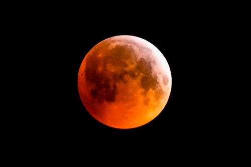 A close-up of a glowing orange full moon against a black sky during a lunar eclipse.