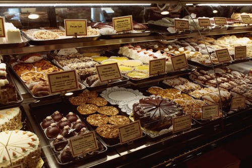 A display case filled with various desserts, including cakes, pies, and cookies, all labeled with names and prices.