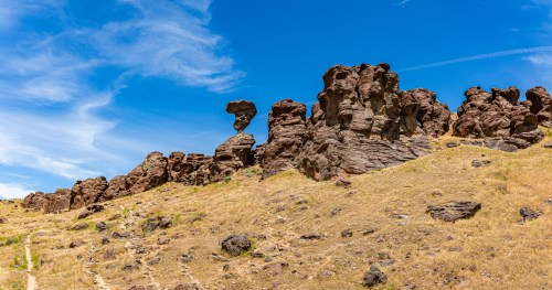 A rocky landscape with unique rock formations under a bright blue sky and scattered clouds.