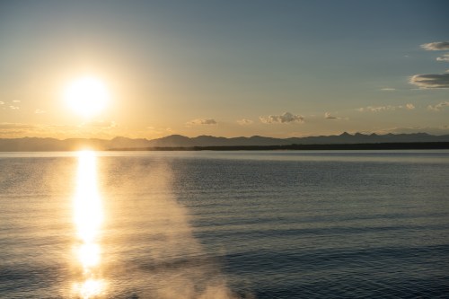 Sunset over a calm lake, with mountains in the distance and a golden reflection on the water's surface.