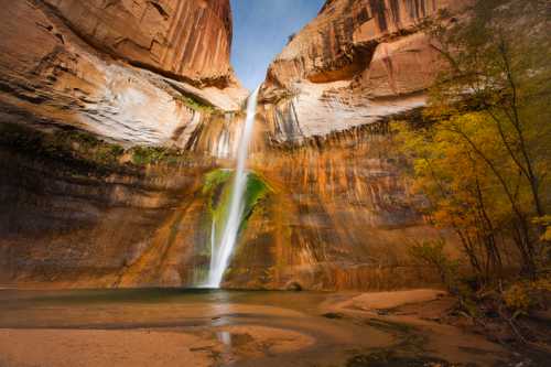 A stunning waterfall cascades down a rocky canyon, surrounded by vibrant autumn foliage and a serene pool below.