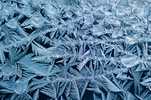 Close-up of intricate frost patterns on a glass surface, showcasing delicate ice crystals and unique textures.