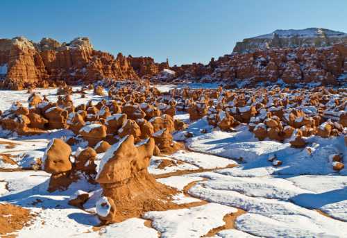 Snow-covered rock formations in a desert landscape under a clear blue sky.