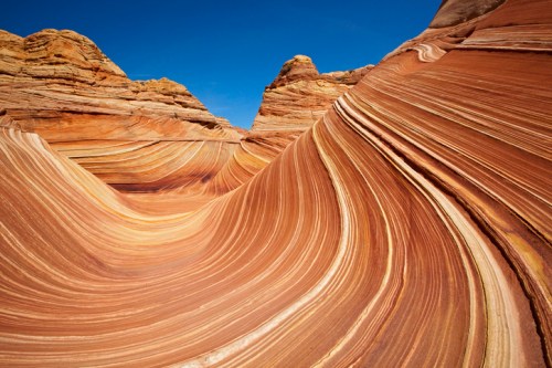 Colorful, undulating rock formations with layered stripes under a clear blue sky.
