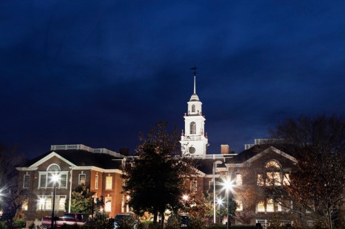 Historic building with a clock tower, illuminated at night against a dark sky. Trees and streetlights in the foreground.