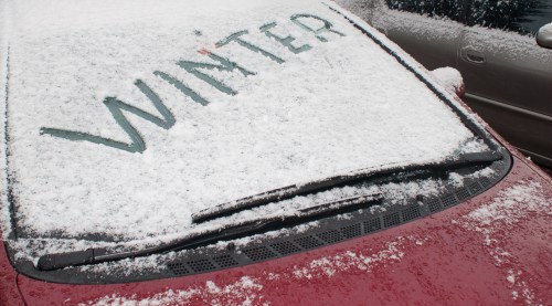 A red car covered in snow with the word "WINTER" written on the windshield.