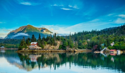 A serene landscape featuring a calm lake, lush greenery, and mountains under a clear blue sky.