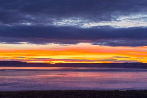 Vibrant sunset over a calm lake, with colorful clouds reflecting on the water's surface.