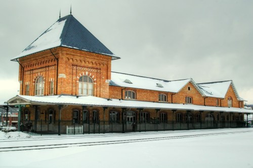 Historic brick train station covered in snow, featuring a tall roof and arched windows under a cloudy sky.