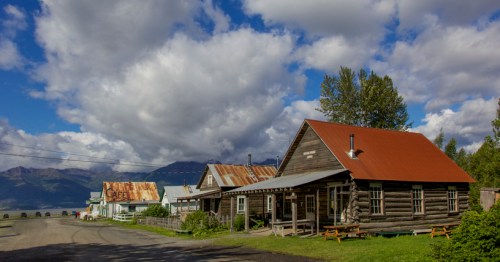 A rustic village scene with wooden houses, a red-roofed cabin, and a backdrop of clouds and mountains.