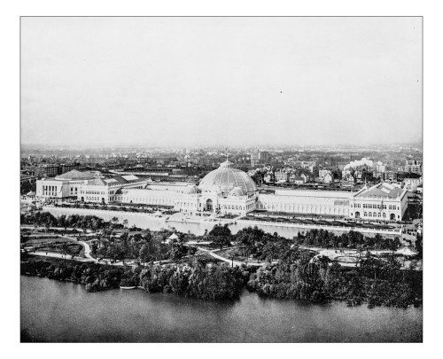 Aerial view of a large historic building with a dome, surrounded by gardens and a river, in black and white.