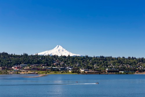A clear blue sky over a snow-capped mountain, with a boat gliding across a calm lake in the foreground.