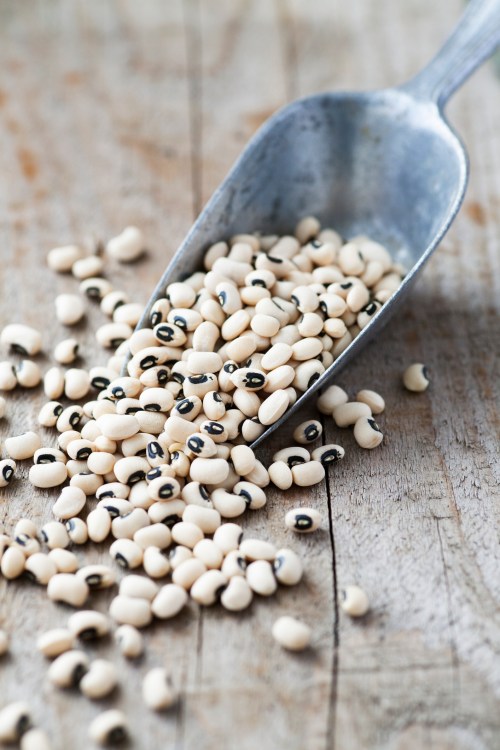 A metal scoop spilling black-eyed peas onto a wooden surface.