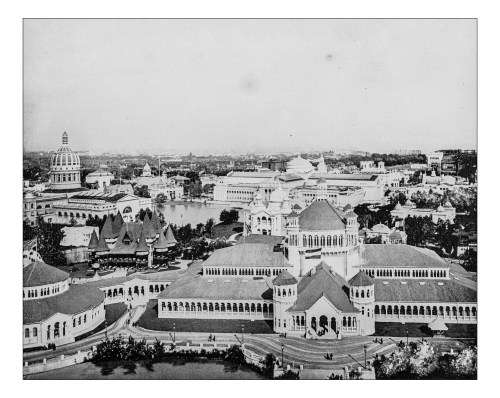 Aerial view of a historic fairground with ornate buildings and a lake, surrounded by trees and pathways.
