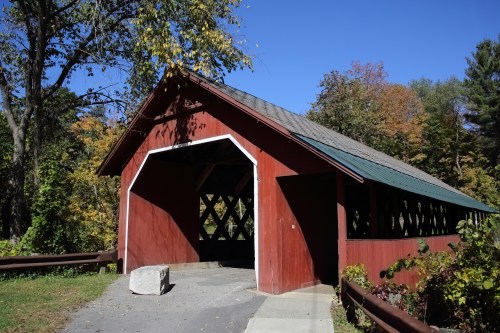 A red covered bridge surrounded by trees with autumn foliage under a clear blue sky.