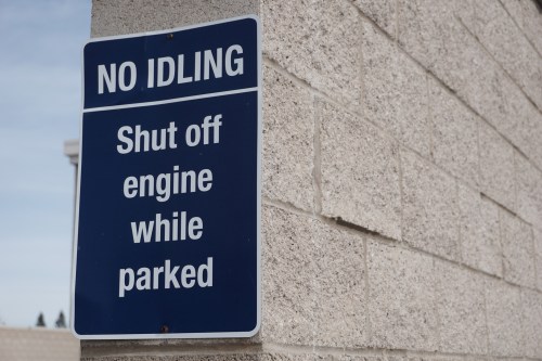 Blue sign on a wall reads "No Idling: Shut off engine while parked."