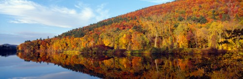 A serene lake reflecting vibrant autumn foliage on a hillside under a clear blue sky.