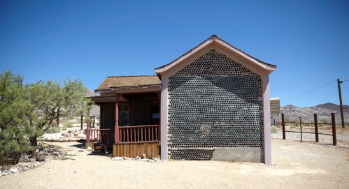 A unique building with a bottle wall, surrounded by desert landscape and clear blue skies.