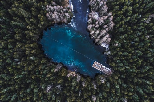 Aerial view of a serene blue lake surrounded by dense green forests and a small dock.