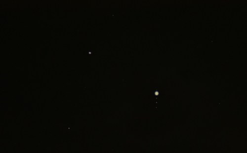 A dark sky filled with stars, featuring a prominent planet with several moons visible nearby.