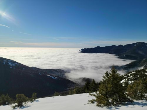 A breathtaking view of mountains above a sea of clouds under a clear blue sky, with snow-covered slopes in the foreground.