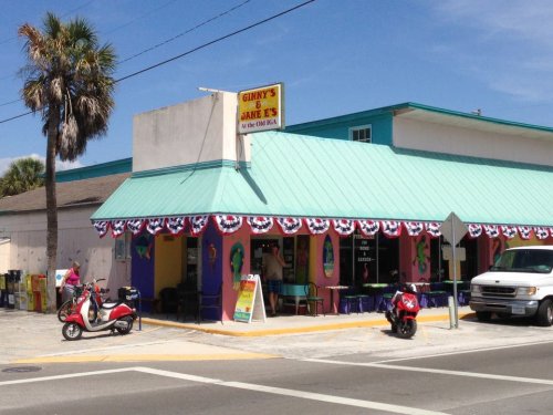 Colorful restaurant with a teal roof, festive bunting, and outdoor seating, located on a sunny street corner.
