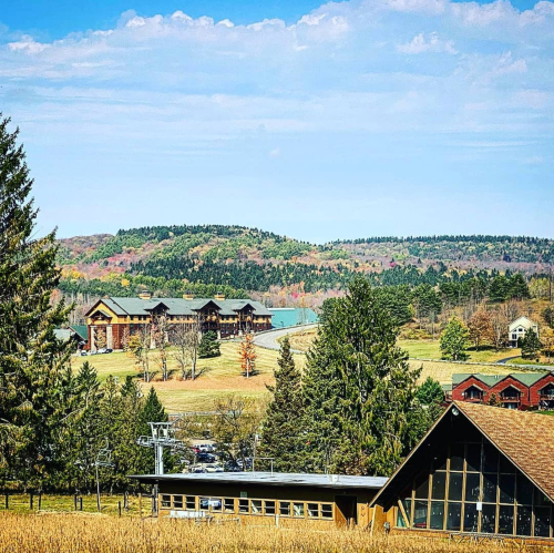 Scenic view of rolling hills with colorful trees, buildings, and a clear blue sky in the background.