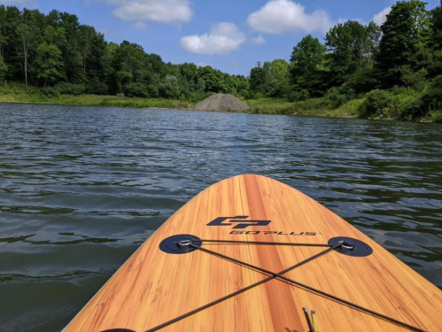 View from a paddleboard on calm water, surrounded by lush greenery and a blue sky with fluffy clouds.