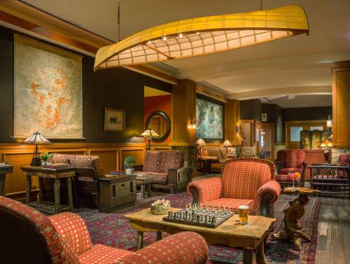 Cozy lounge with red patterned chairs, wooden tables, a chess set, and warm lighting, adorned with maps on the walls.