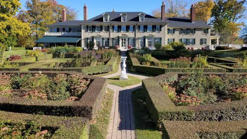 A large, elegant house surrounded by neatly trimmed hedges and colorful gardens on a sunny day.