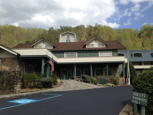 A charming lodge with a stone facade, surrounded by greenery, featuring a flag and a "Guests Parking Only" sign.