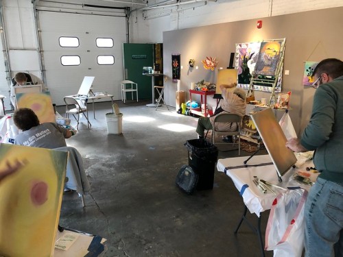 Artists painting on canvases in a spacious studio with various artworks displayed on the walls.