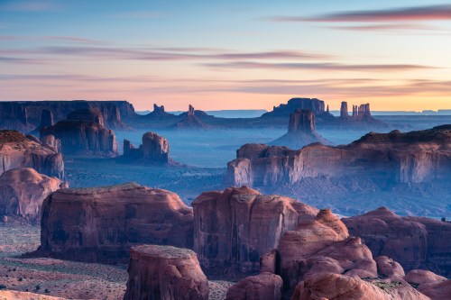 A stunning desert landscape at sunrise, featuring towering rock formations and a colorful sky.