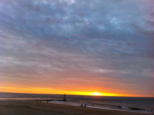 A serene beach scene at sunset, with vibrant orange hues in the sky and gentle waves lapping at the shore.