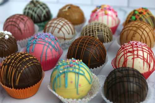 A colorful assortment of chocolate-covered dessert balls in various flavors, decorated with sprinkles and drizzles.