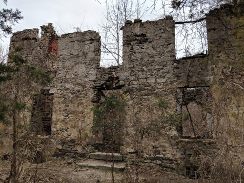 Ruins of a stone building overgrown with vegetation, featuring crumbling walls and empty window frames.