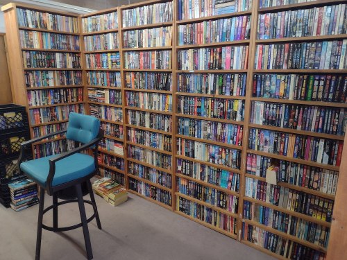 A cozy room with tall bookshelves filled with books and a teal barstool in front.