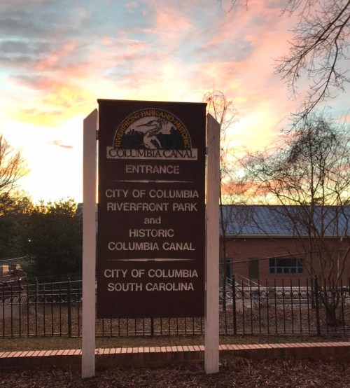 Sign for Columbia Canal entrance at Riverfront Park, Columbia, South Carolina, with a sunset in the background.