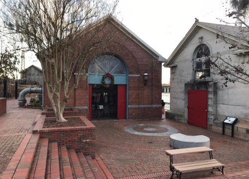 Brick building with arched windows, red doors, and a festive wreath, surrounded by a circular brick pathway and benches.