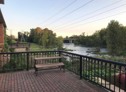 A peaceful riverside view with trees, a bench, and power lines under a clear sky at sunset.