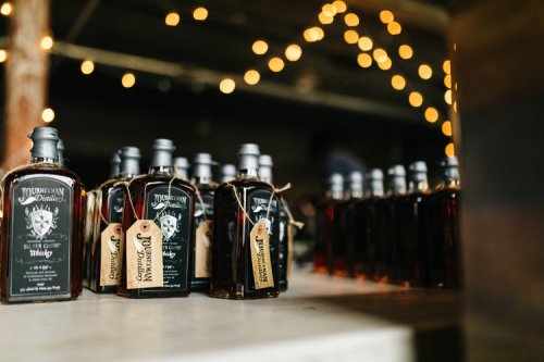 Bottles of whiskey lined up on a table, with warm string lights in the background creating a cozy atmosphere.