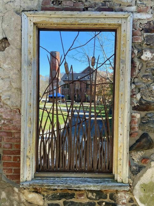 A rustic window frame with metal grass designs, reflecting a building and trees outside.