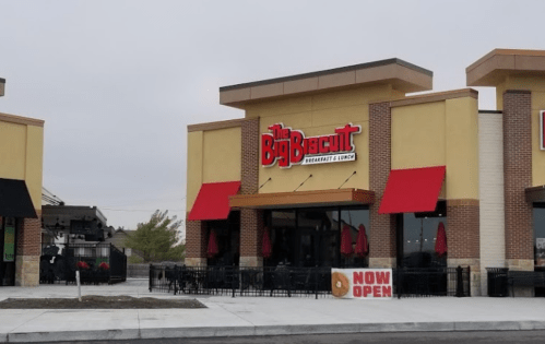 Exterior of The Big Biscuit restaurant with a "Now Open" sign and outdoor seating area.