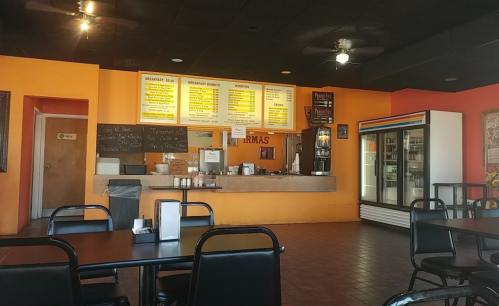 Interior of a casual restaurant featuring a counter with a menu, seating area, and vibrant orange walls.
