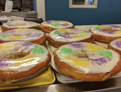 A tray of colorful king cakes, decorated with purple, green, and yellow sprinkles, wrapped in plastic.
