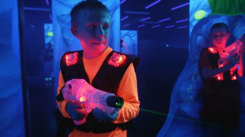 A young boy in a neon-lit laser tag arena holds a laser gun, focused and ready to play.