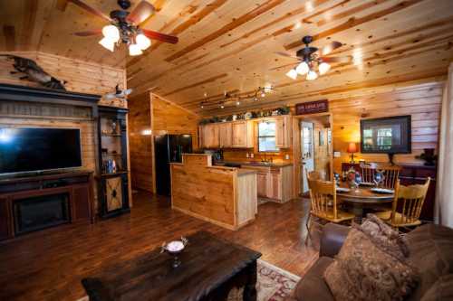 Cozy wooden interior of a cabin featuring a living area, kitchen, dining table, and warm lighting.