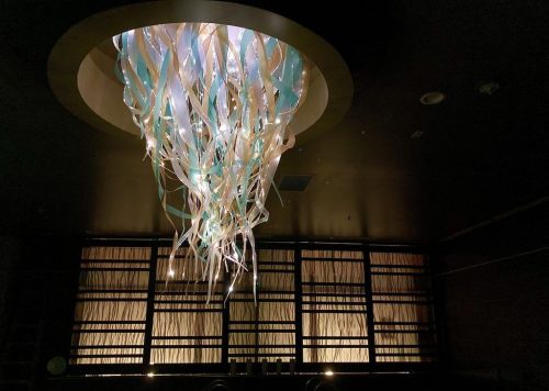 A modern chandelier with flowing ribbons of light hangs in a dimly lit room with textured walls.